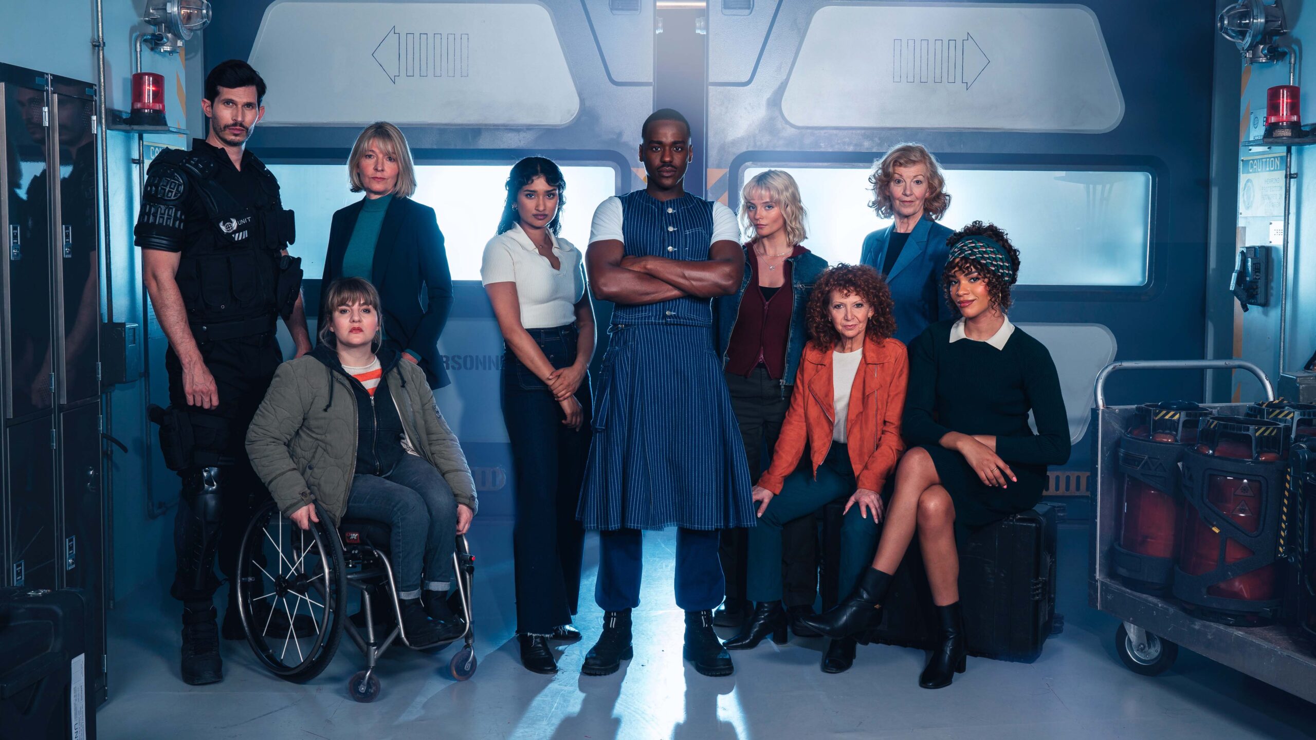 Alexander Devient, Jemma Redgrave, Ruth Madeley, Varada Sethu, Ncuti Gatwa, Millie Gibson, Bonnie Langford, Susan Twist, Yasmin Finley no cenário de Reality War, em foto para divulgação do episódio.